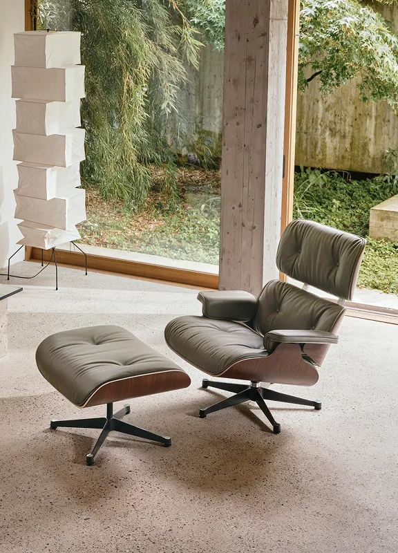 Gemütlicher Wohnraum mit Eames Lounge Chair in Nussbaum und Leder, Ottoman, Papierlampe und Gartenblick.