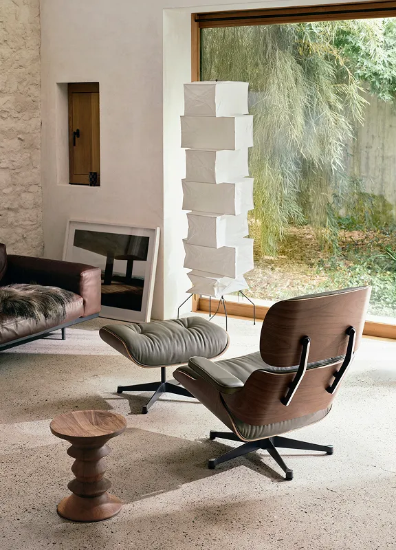 Moderner Wohnraum mit Eames Lounge Chair und Ottoman von hinten, Holzdetails, Leder, Papierlampe und großem Fenster zum Garten.